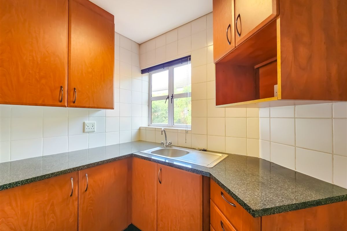 A compact office kitchenette featuring wooden cabinetry, granite-look countertops, a stainless steel sink, and tiled splashbacks.