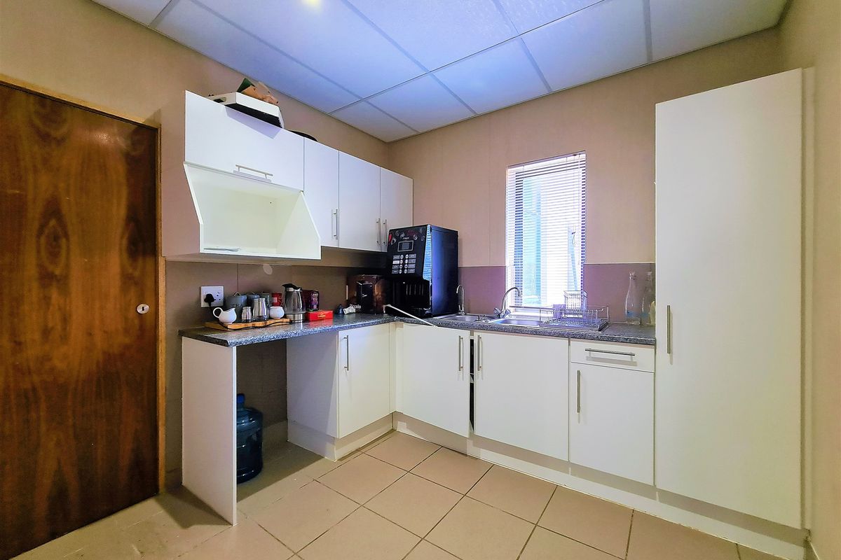 A functional office kitchenette featuring white cabinetry, a stainless steel sink, tiled flooring, and a drop ceiling with integrated lighting.