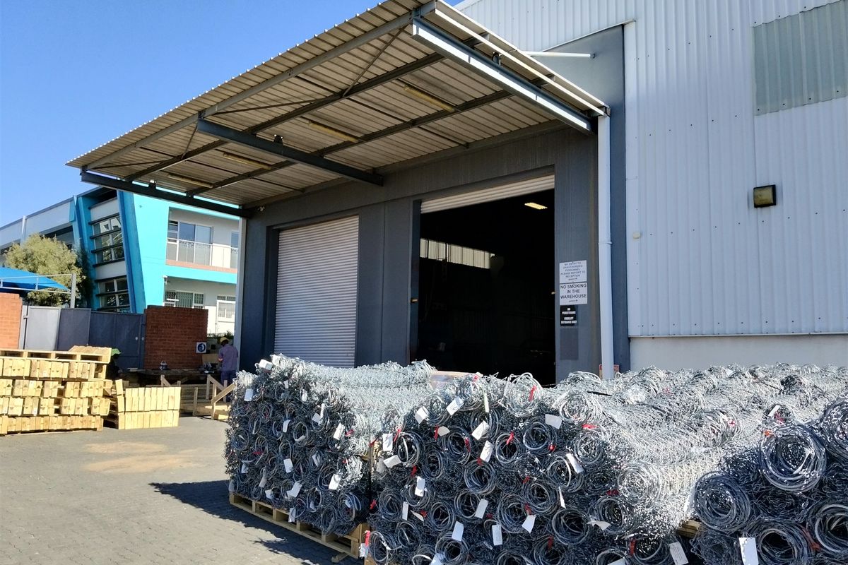 Industrial warehouse exterior featuring a large roller shutter door, covered loading bay canopy, and corrugated metal cladding.