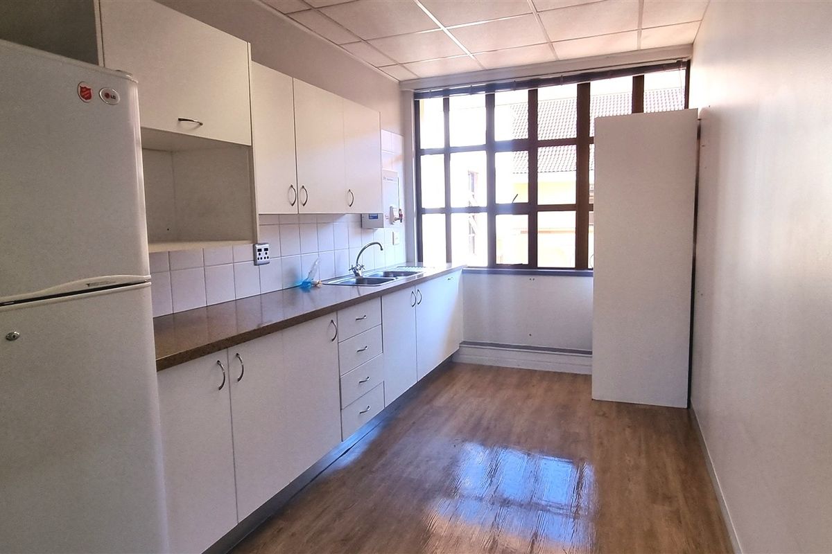 A functional office kitchenette featuring white cabinetry, a stainless steel sink, laminate countertops, and a large window providing natural light.