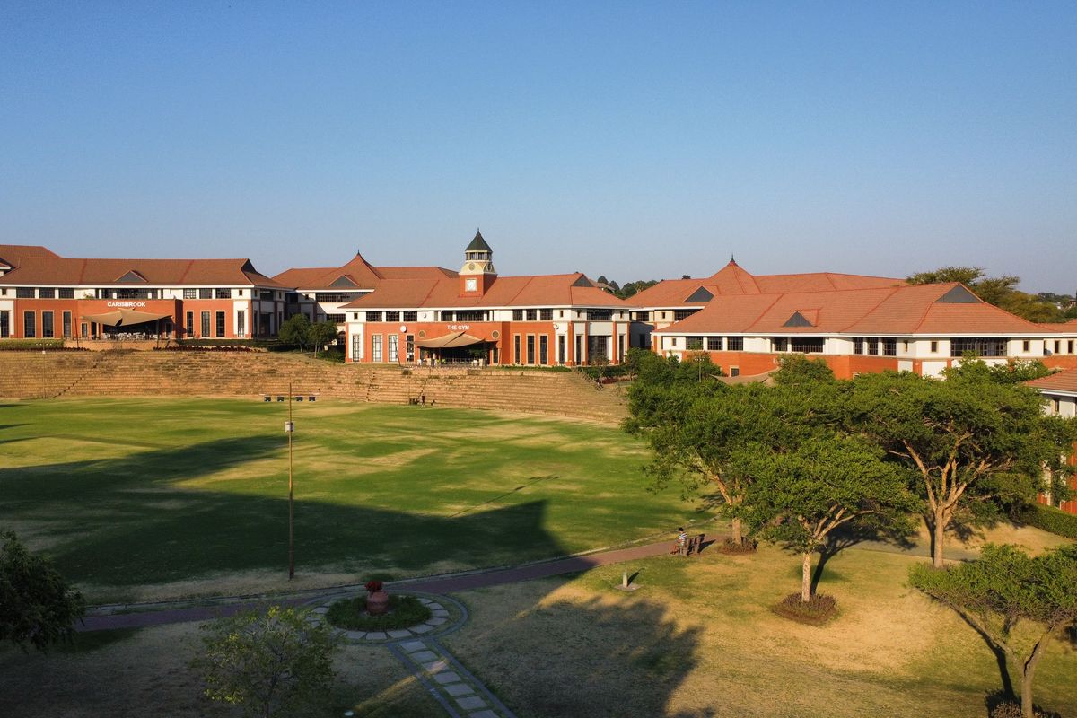 Aerial view of a large office complex featuring multiple brick buildings with terracotta tiled roofs, surrounding a central landscaped lawn and sports field.