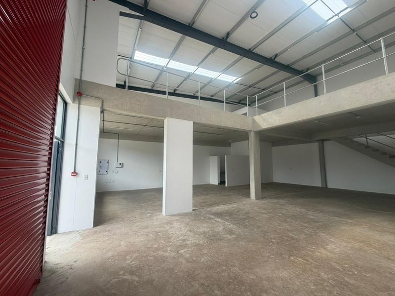 Spacious industrial unit featuring a mezzanine level, concrete flooring, high ceilings with skylights, and a large roller shutter door for easy access.