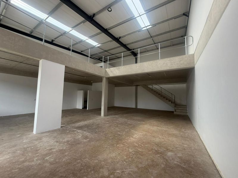 Spacious industrial open-plan unit featuring a mezzanine level, concrete flooring, exposed steel roof trusses, and natural light from overhead skylights.