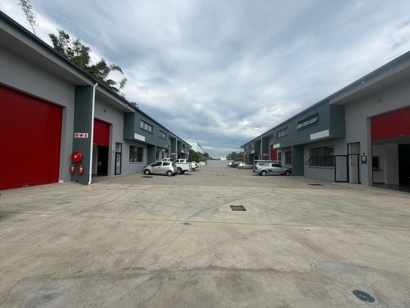 A view of an industrial complex courtyard featuring multiple units with red roller shutter doors and a paved concrete driveway.