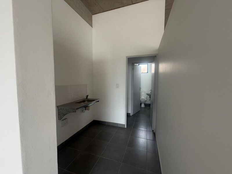 A functional utility area featuring a stainless steel sink, tiled flooring, and an exposed concrete ceiling, with an adjacent bathroom visible.