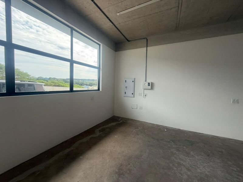 An empty industrial-style office space featuring exposed concrete ceilings, polished concrete flooring, and large windows providing natural light.