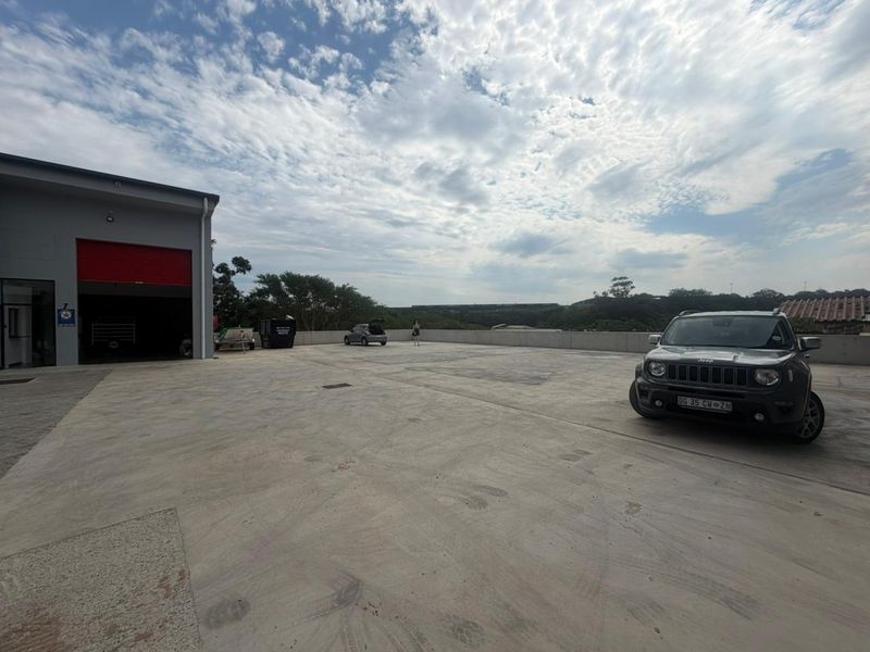 Spacious industrial concrete yard area featuring a large roller shutter door access point and perimeter retaining wall.