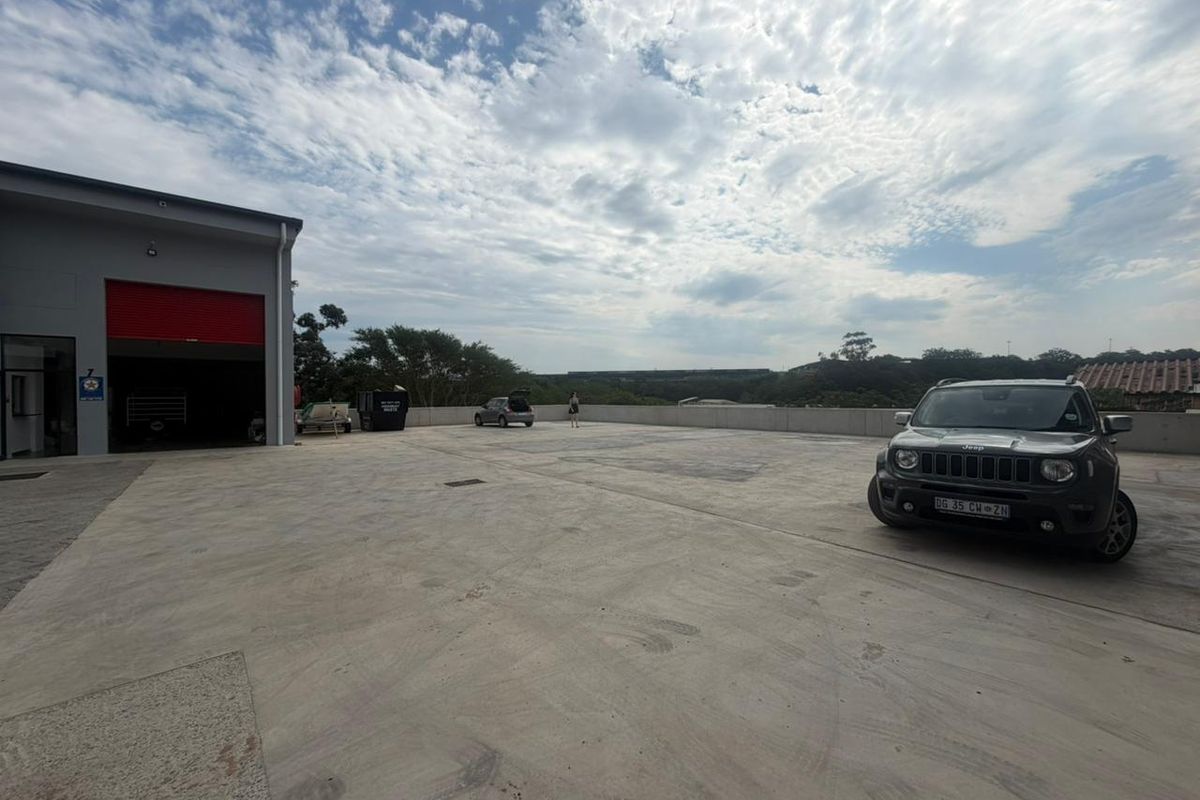 Spacious industrial concrete yard area featuring a large roller shutter door access point and perimeter retaining wall.