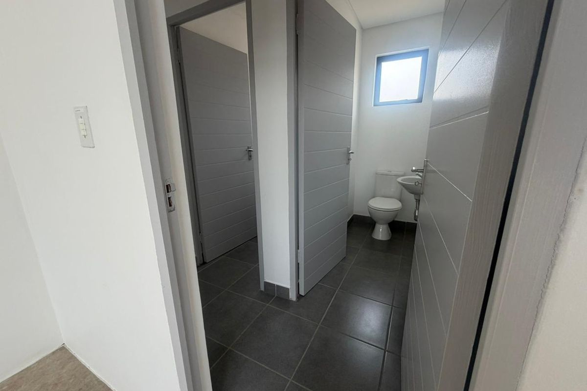 A clean, modern bathroom featuring tiled flooring, a toilet, and a wall-mounted basin, accessible via internal doors.