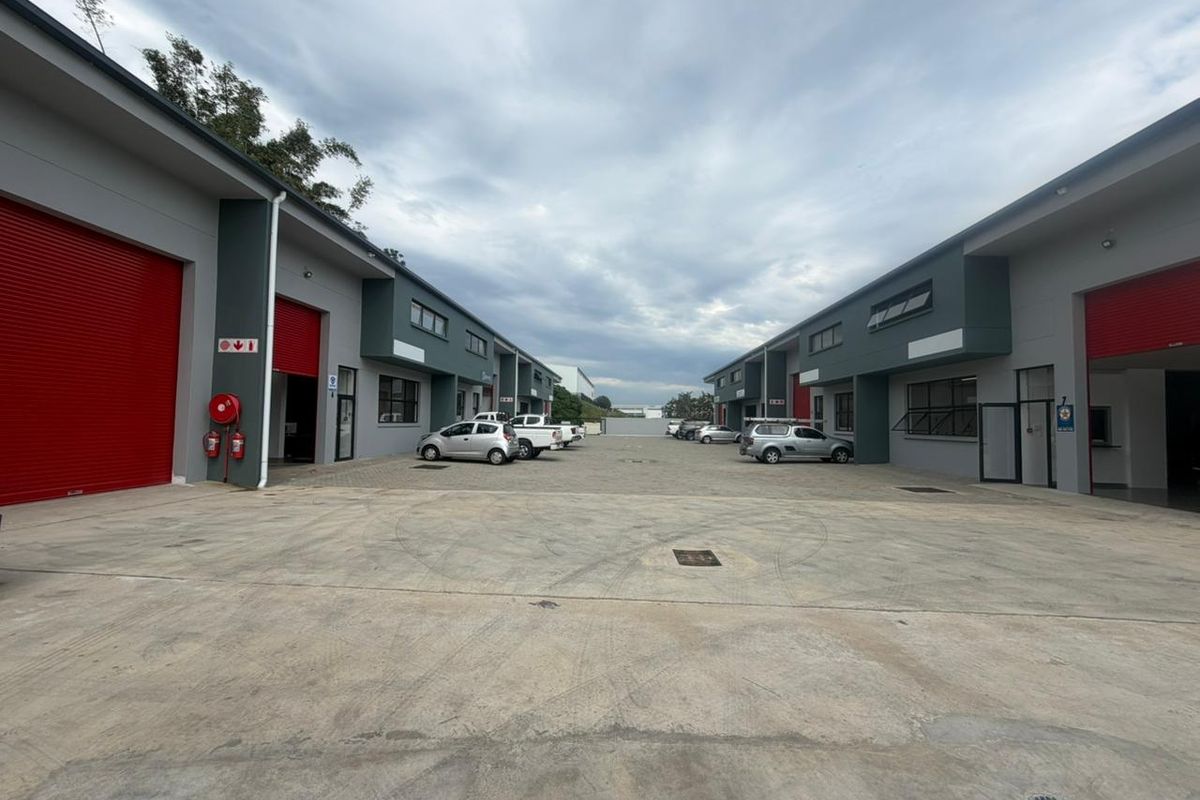 A view of an industrial complex courtyard featuring multiple units with red roller shutter doors and a paved concrete driveway.