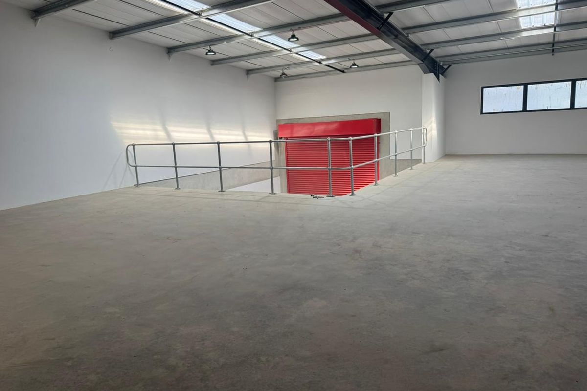 Spacious industrial mezzanine area featuring concrete flooring, exposed steel roof trusses, skylights, and a secure red metal roller shutter door.