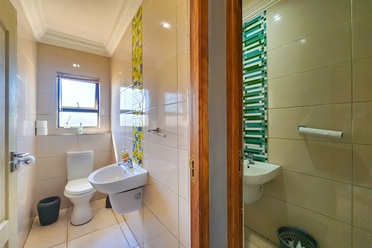 A functional office bathroom featuring tiled walls with decorative mosaic accents, a wall-mounted basin, and a standard toilet suite.