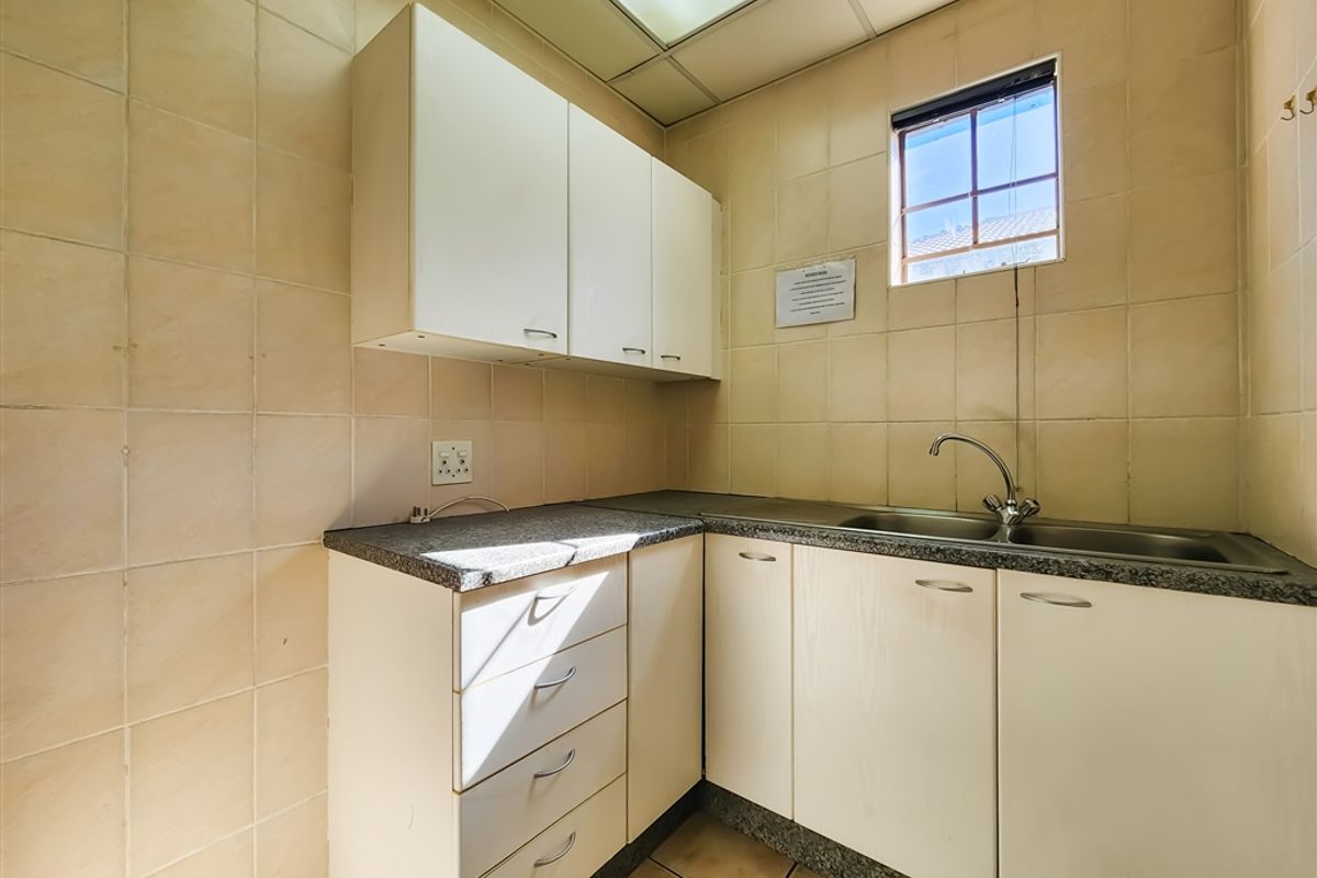 A functional office kitchenette featuring built-in cabinetry, a stainless steel sink, granite-look countertops, and full wall tiling.