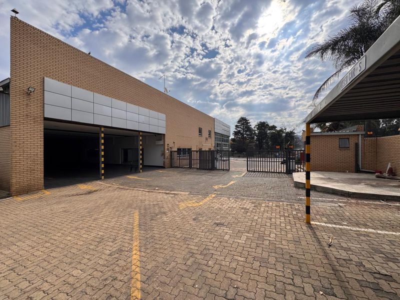 Front exterior view of a retail property featuring a paved driveway, covered parking area, and secure metal gate access.