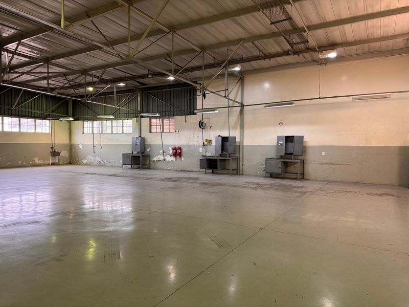 Spacious industrial utility area featuring exposed steel roof trusses, concrete flooring, and fixed metal workstations, suitable for workshop or storage use.