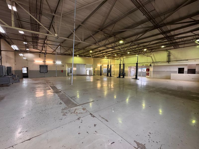 Spacious industrial workshop featuring high ceilings with exposed steel trusses, durable epoxy-coated flooring, and integrated vehicle service lifts.