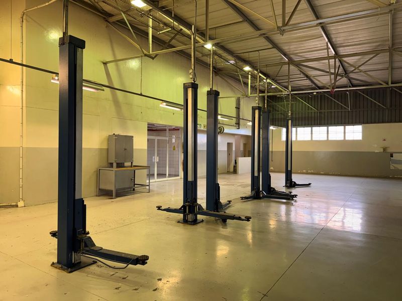 Spacious industrial garage facility featuring multiple built-in vehicle lifts, high ceilings with exposed steel trusses, and durable epoxy-coated flooring.