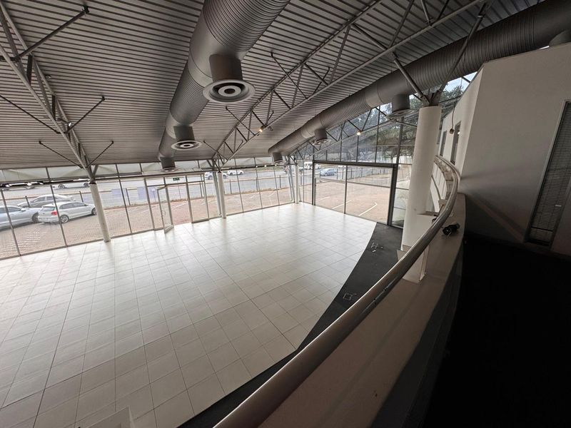 Spacious open-plan retail area featuring high ceilings with exposed ducting, large glass windows, and tiled flooring, offering excellent visibility and natural light.