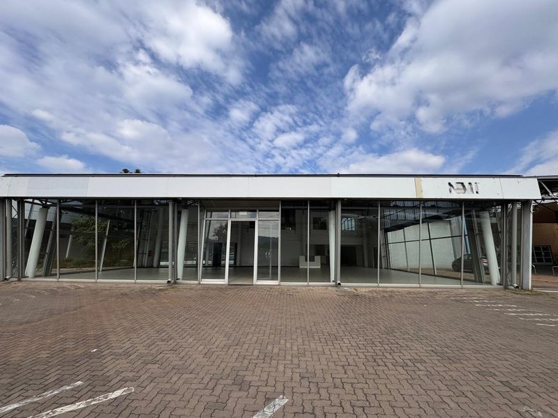 Front elevation of a commercial retail property featuring a large glass facade, structural steel supports, and an expansive paved parking area.