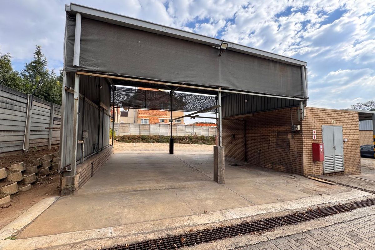 An open-sided utility or service bay featuring a concrete floor, brick walls, and a metal roof structure, suitable for various commercial or storage purposes.