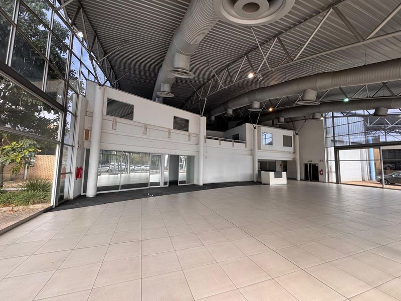 Spacious open-plan retail area featuring high ceilings with exposed ducting, large glass windows, tiled flooring, and a mezzanine level for versatile commercial use.