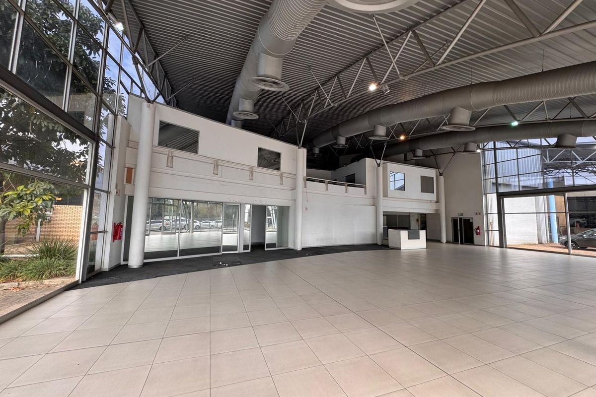 Spacious open-plan retail area featuring high ceilings with exposed ducting, large glass windows, tiled flooring, and a mezzanine level for versatile commercial use.