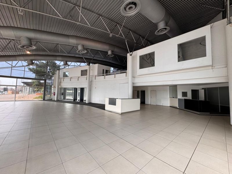 Spacious open-plan retail area featuring high ceilings with exposed ductwork, tiled flooring, a built-in reception desk, and a mezzanine level.