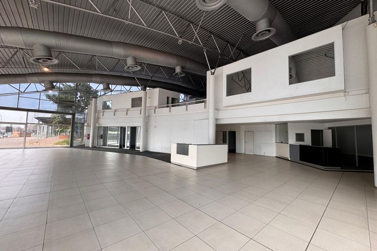 Spacious open-plan retail area featuring high ceilings with exposed ductwork, tiled flooring, a built-in reception desk, and a mezzanine level.