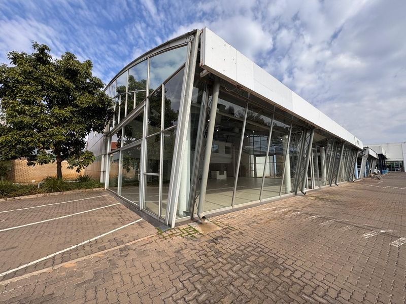 Modern retail building featuring an expansive glass curtain wall facade, steel structural framing, and dedicated paved parking area.