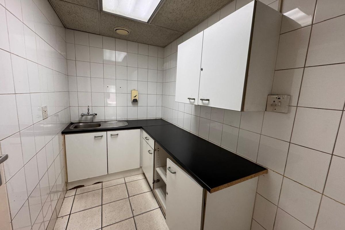 A functional kitchenette featuring white cabinetry, black laminate countertops, a stainless steel sink, and fully tiled walls and floors.