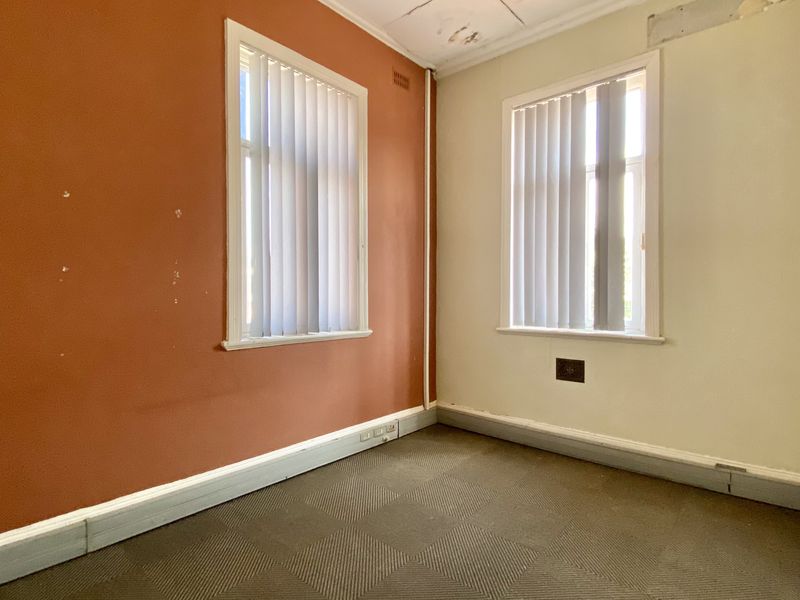 An empty office space featuring carpet flooring, vertical blinds, and dual windows, requiring cosmetic updates to the walls and ceiling.
