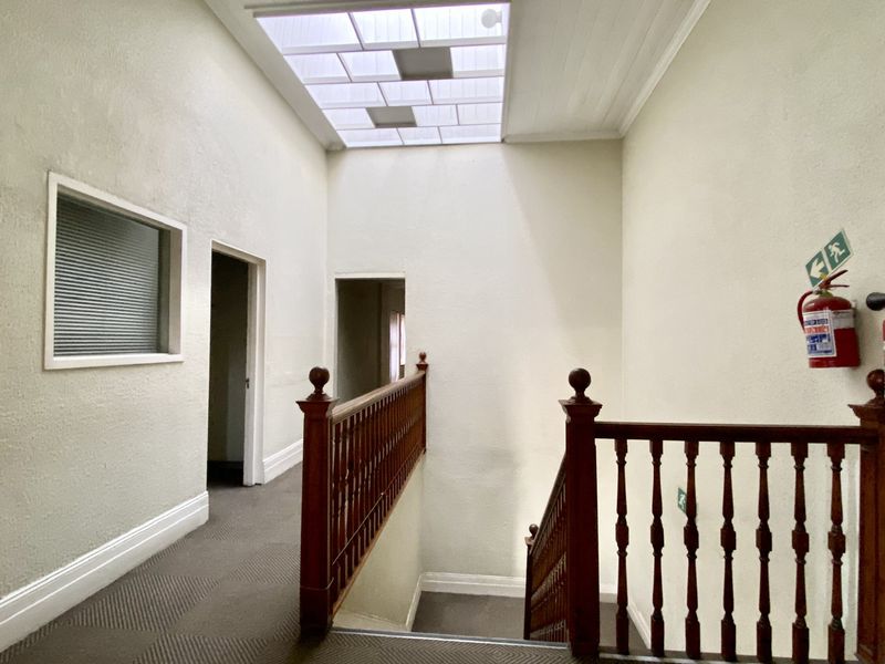 A bright commercial hallway featuring a large skylight, wooden balustrade, and staircase access, equipped with essential fire safety equipment.