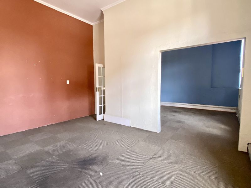 An empty open-plan commercial space featuring carpet tile flooring, a french door, and distinctively painted walls, ready for custom fit-out.