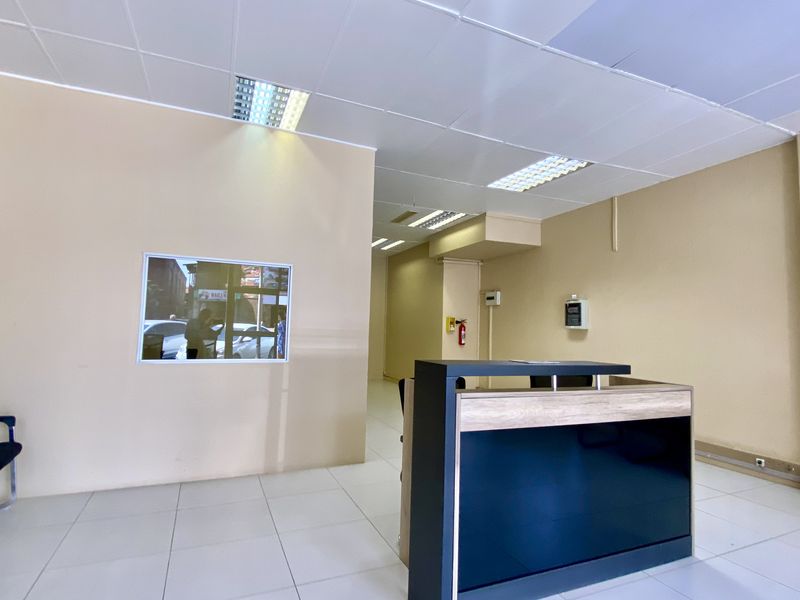 A clean, functional commercial office space featuring a reception desk, tiled flooring, and a suspended ceiling with recessed lighting.