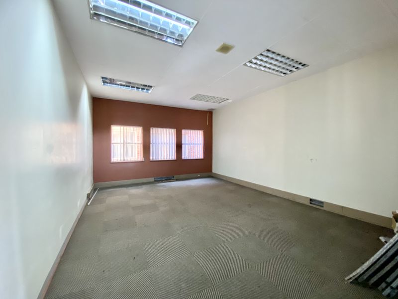 An empty commercial office space featuring recessed fluorescent lighting, carpeted flooring, and windows fitted with security bars.