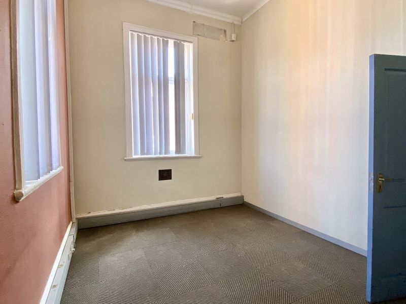 An empty office space featuring carpeted flooring, vertical blinds, and neutral wall finishes, suitable for a professional workspace or small commercial studio.