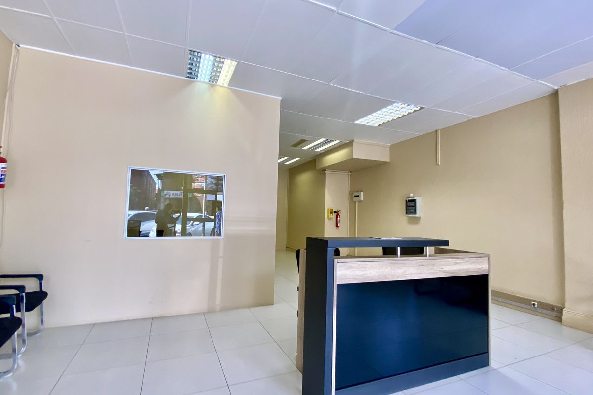 A clean, functional commercial office space featuring a reception desk, tiled flooring, and a suspended ceiling with recessed lighting.