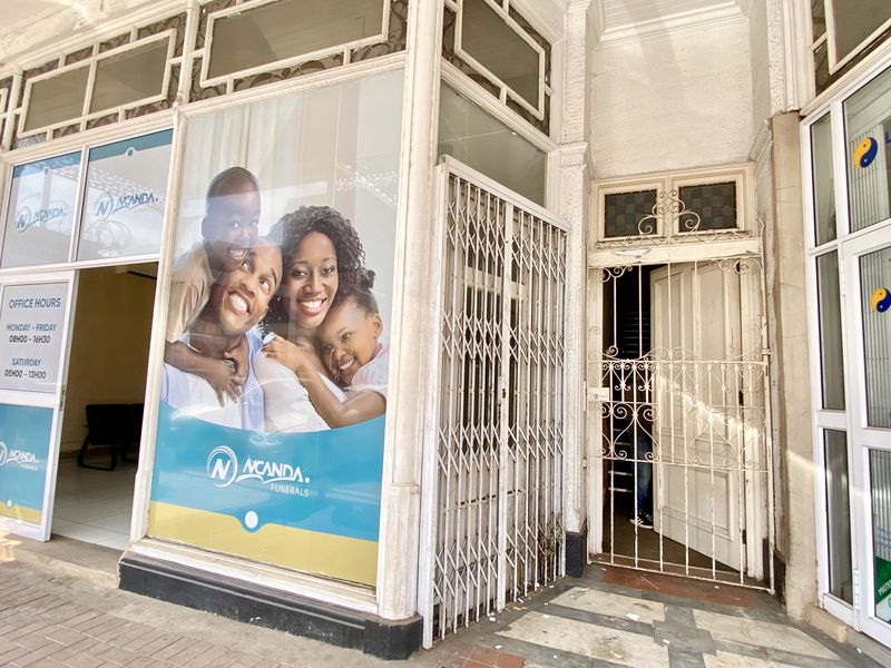 Commercial storefront entrance featuring large glass display windows, security gates, and tiled access area, currently occupied by a funeral services business.