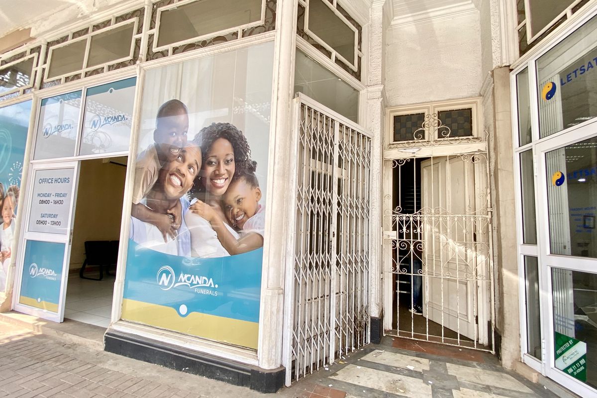 Commercial storefront entrance featuring large glass display windows, security gates, and tiled access area, currently occupied by a funeral services business.