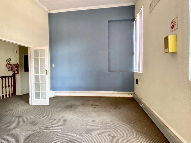 An empty office space featuring carpeted flooring, a blue accent wall with a recessed niche, and double french doors leading to a staircase.