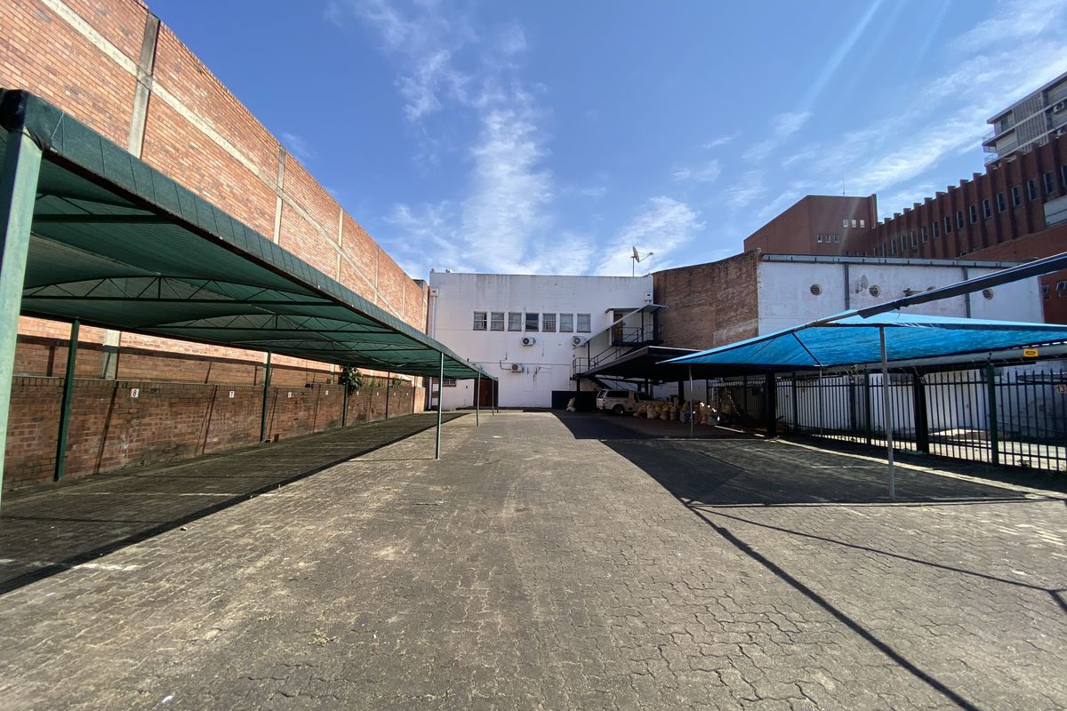 Commercial rear exterior area featuring a large paved parking lot with multiple shade cloth carports and perimeter brick boundary walls.