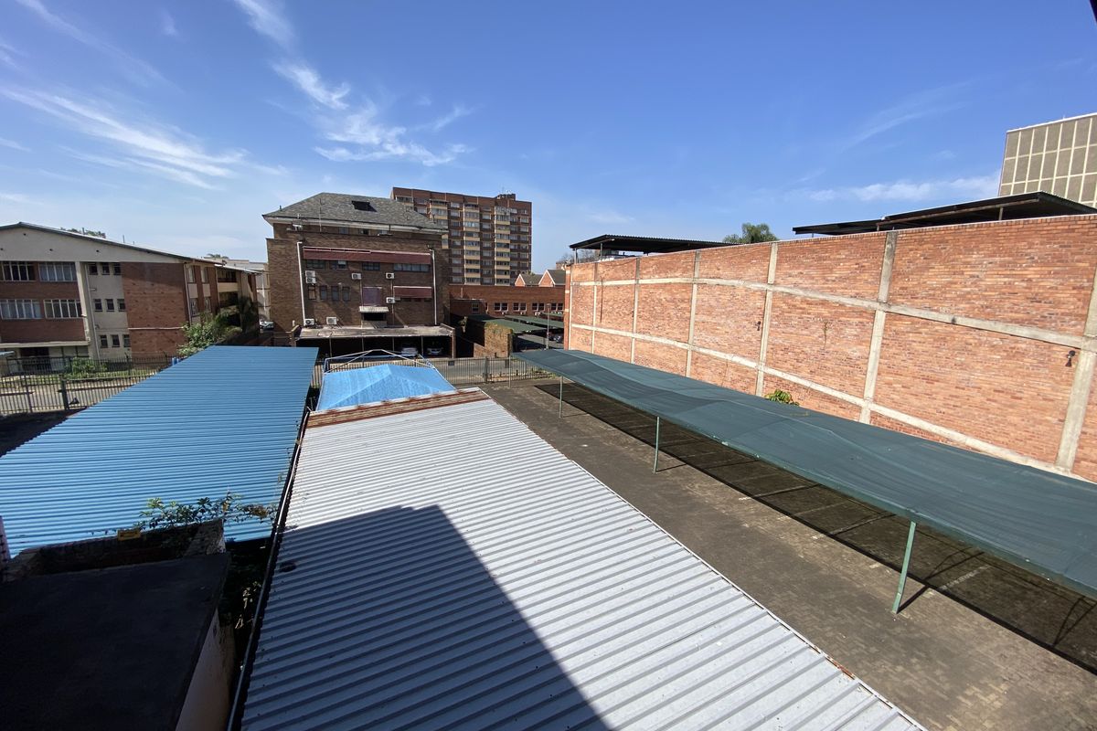 Aerial view of the commercial property grounds featuring multiple corrugated metal roof structures, shade cloth carports, and a brick boundary wall.