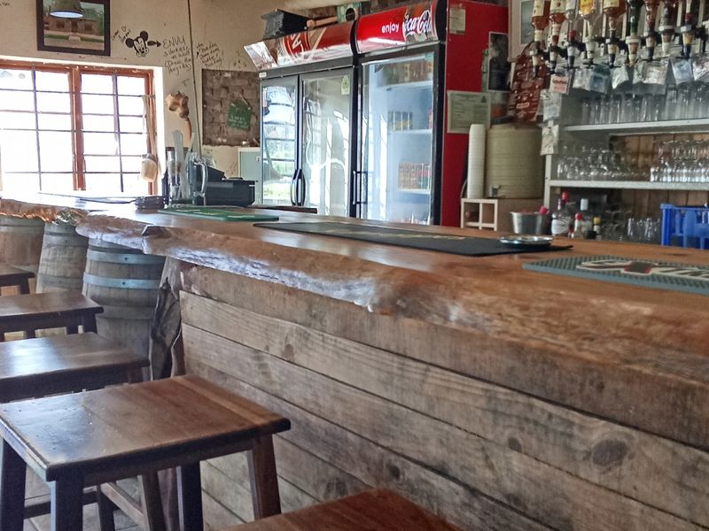 A rustic bar area featuring a wooden counter, integrated beverage refrigeration, and shelving for glassware, showing signs of wear and wall markings.