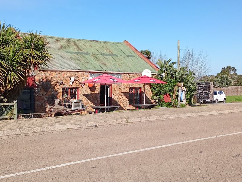 Front exterior view of a rustic stone-clad restaurant building featuring a corrugated metal roof and adjacent paved sidewalk.