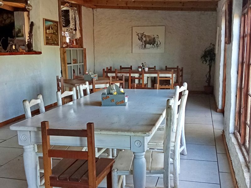 Rustic dining area featuring exposed timber ceiling beams, tiled flooring, and large timber-framed windows providing natural light.