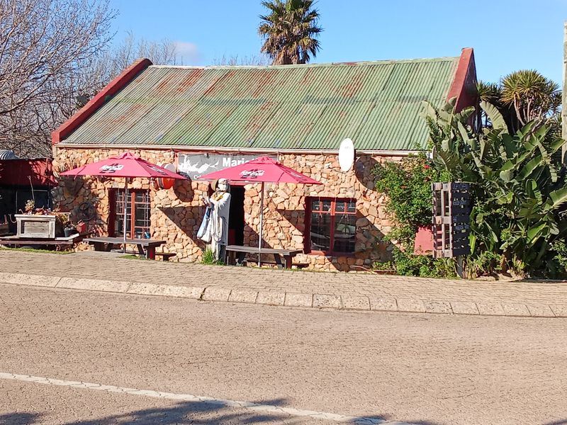 A rustic stone-clad restaurant building featuring a corrugated metal roof and timber-framed windows, situated along a paved street.