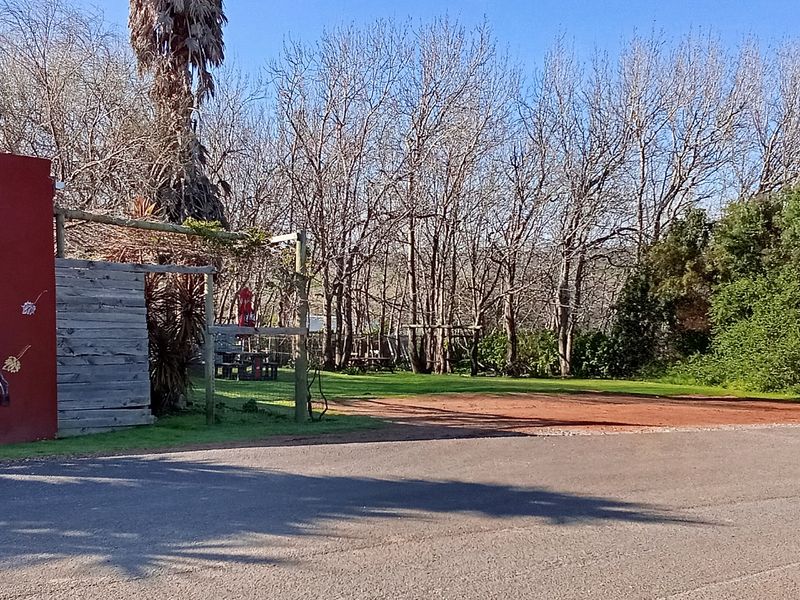 A rear exterior view of the restaurant property featuring a painted masonry wall, timber pergola, and an open gravel parking area adjacent to garden space.