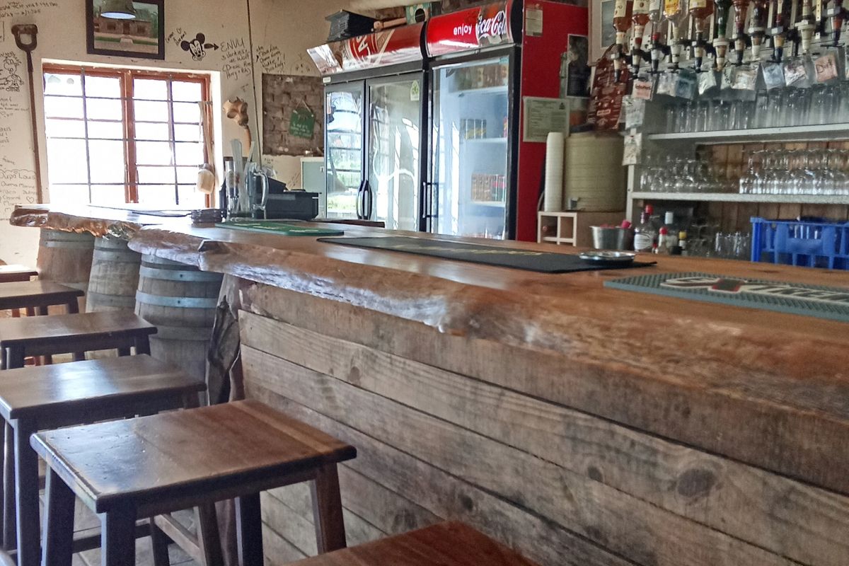 A rustic bar area featuring a wooden counter, integrated beverage refrigeration, and shelving for glassware, showing signs of wear and wall markings.