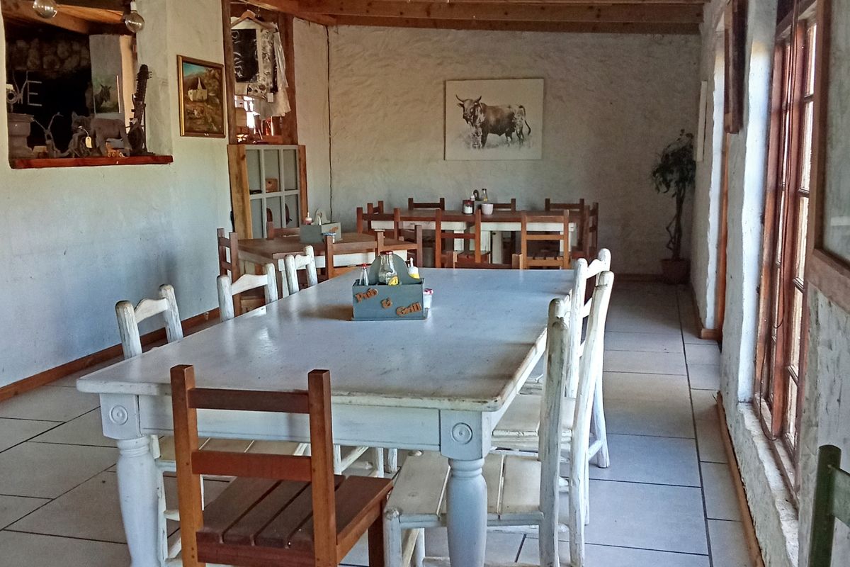 Rustic dining area featuring exposed timber ceiling beams, tiled flooring, and large timber-framed windows providing natural light.