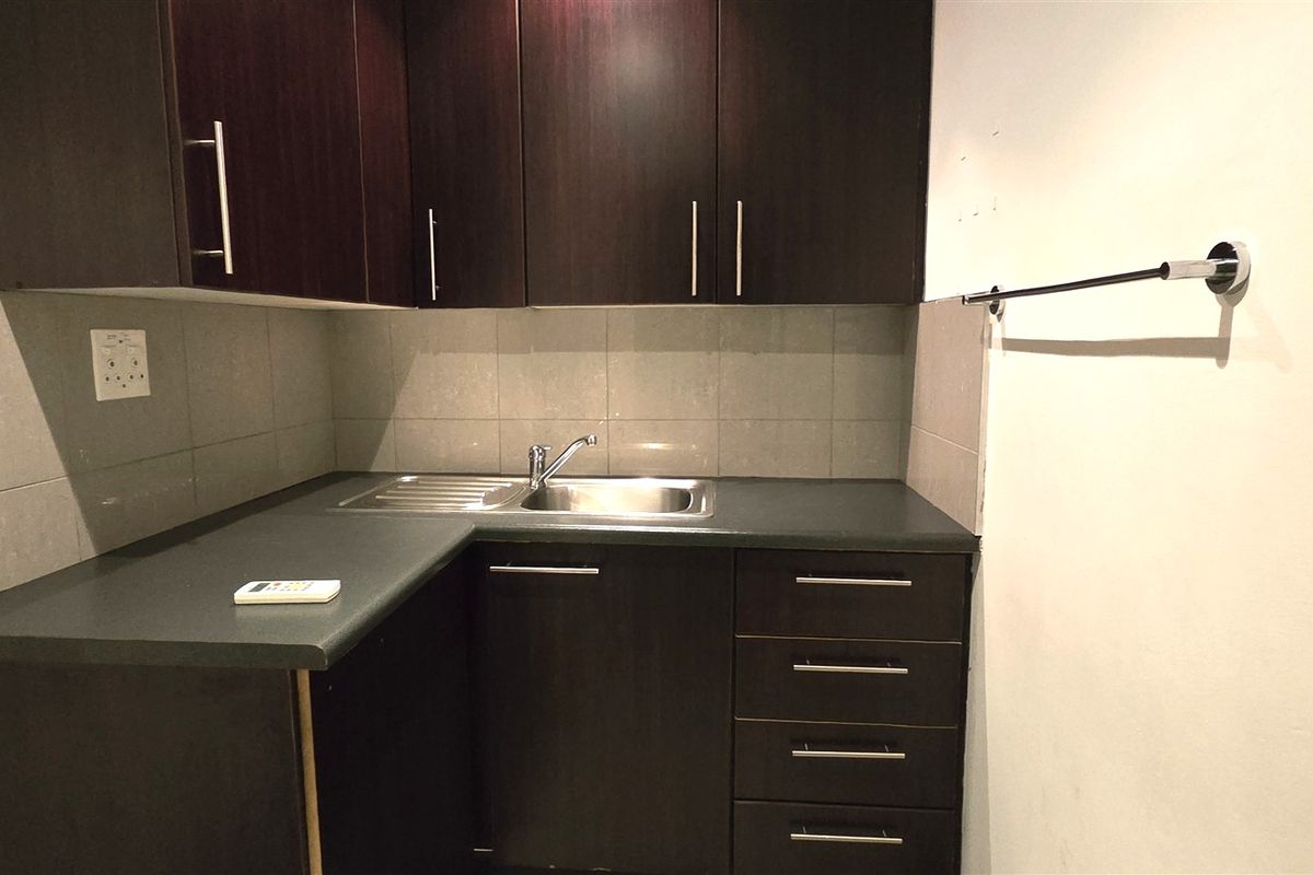 Compact kitchenette featuring dark wood-finish cabinetry, a stainless steel sink, and tiled splashback, suitable for an office break area.